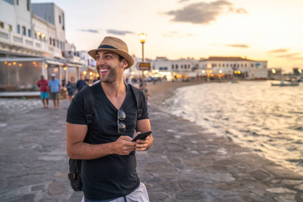 istock Young Man Looking At View And Holding Smartphone in Mykonos, Greece 1166996771
