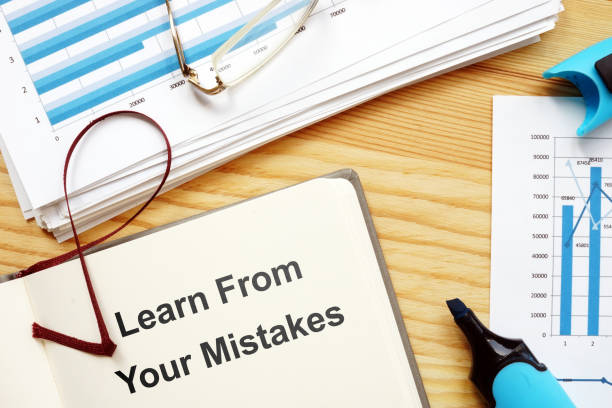 istock Writing note showing Learn From Your Mistakes. The text is written on a paper of notebook. Papers with graphs and colored papers, markers, wooden background are on the photo too. 1166998516