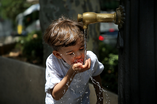 A young Muslim man drinking water from running pipe.