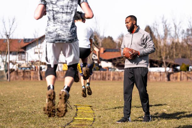 Adult black man holding a ball for american football and training young male athletes.