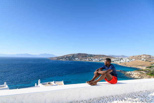 The African man sits on a white wall and admires the view.