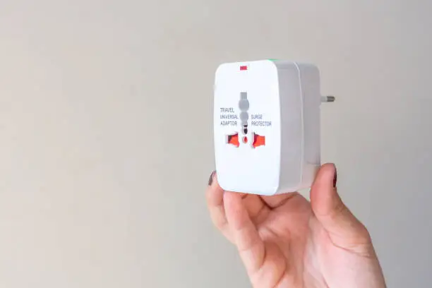 A woman's hand holds a travel adapter on white background.