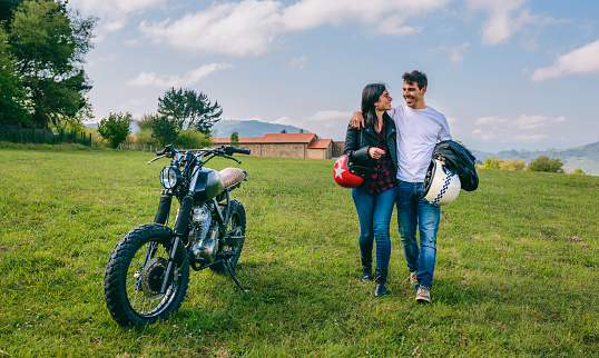 Unrecognizable couple walking on the field embraced and parked motorbike