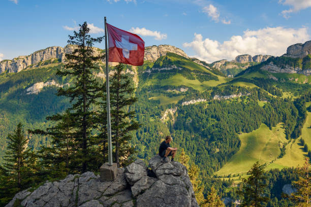 Tourist sitting on the Ebenalp mountain in the Swiss Alps of Switzerland Tourist enjoys spectacular views over Appenzell Alps under Swiss flag sitting on the Ebenalp mountain in the Swiss Alps of Switzerland. appenzell stock pictures, royalty-free photos & images