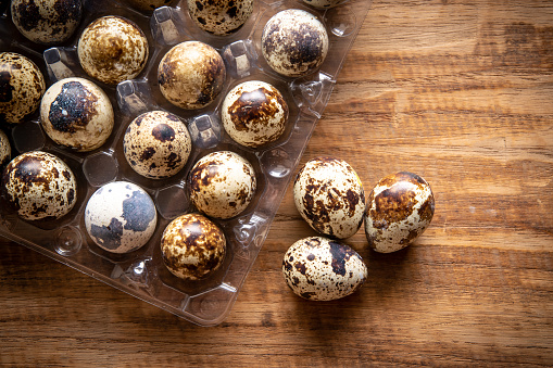 Quail eggs in plastic container on wooden background from supermarket