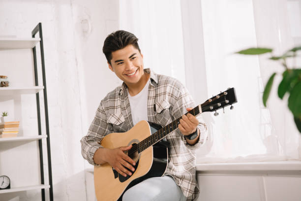 istock handsome, young asian man looking away while playing acoustic guitar at home 1167019057
