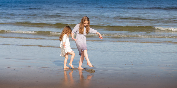 Lifestyle photo of two little sisters having fun playing on a beach in Kennebunkport, Maine in the summer.