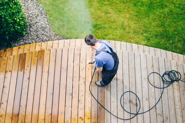 Photo of cleaning terrace with a power washer - high water pressure cleaner on wooden terrace surface