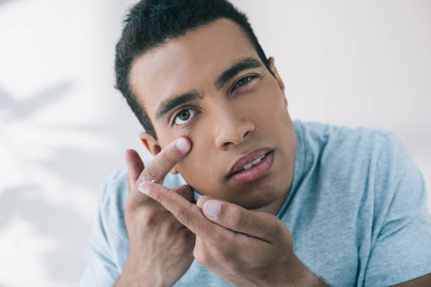 istock young man trying to put contact lens in eye while looking at camera 1167036710