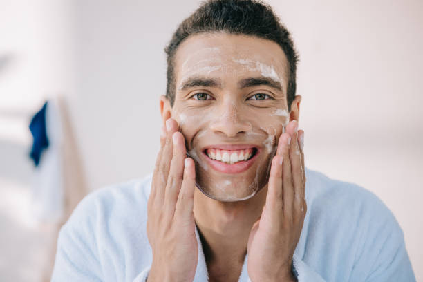 istock handsome young man in bathrobe applying facial foam with hands and smiling while looking at camera 1167036741