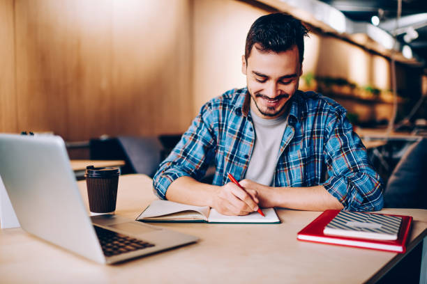 istock Smiling male blogger satisfied with having great idea for publication making notes sitting at desktop with netbook, positive student enjoying learning process doing homework task in college library 1167037650