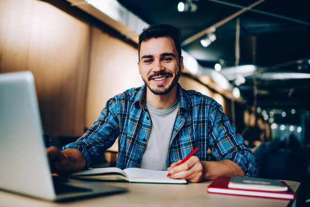 istock Portrait of cheerful male student enjoying learning in coworking office using laptop computer for research,happy freelancer looking at camera during making project for remote job making notes 1167037657