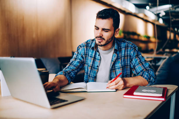 istock Male student browse information for studying language via online courses on netbook in coworking office, hipster guy using laptop computer writing article in notepad for publication in social networks 1167037914