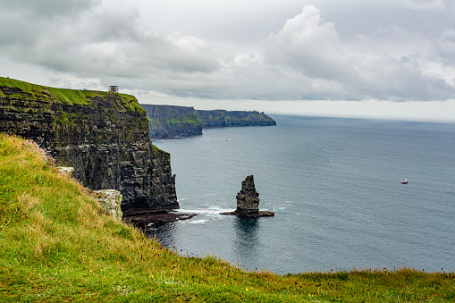 Landscape of the Cliffs of Moher and the Branaunmore sea stack with boats sailing in the ocean, geosites and geopark, Wild Atlantic Way, wonderful cloudy spring day in County Clare in Ireland