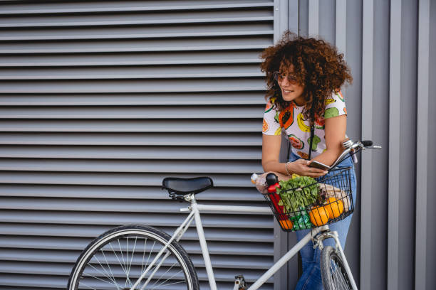 eine junge frau macht eine pause vom radfahren und nutzt handy - fahrradkorb stock-fotos und bilder