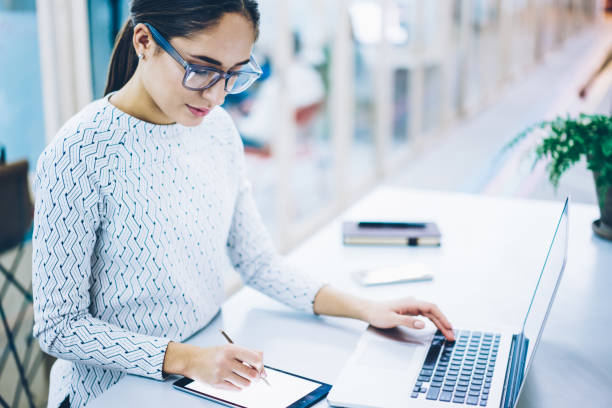istock Experienced woman secretary signing documents via touchpad app synchronizing with netbook, skilled female administrative manager making plannings on digital tablet organizing working process 1167040564