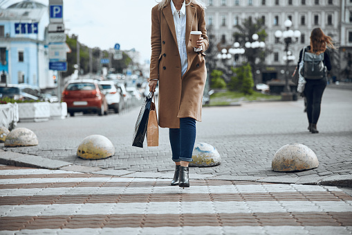 Cropped photo of the elegant woman with coffee in paper cup crossing the road