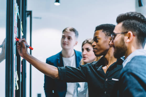 istock Diverse team of skilled students together solving task writing down information on papers glued on wall.Multicultural young people collaborating on business plan making notes of ideas on sticker 1167050262