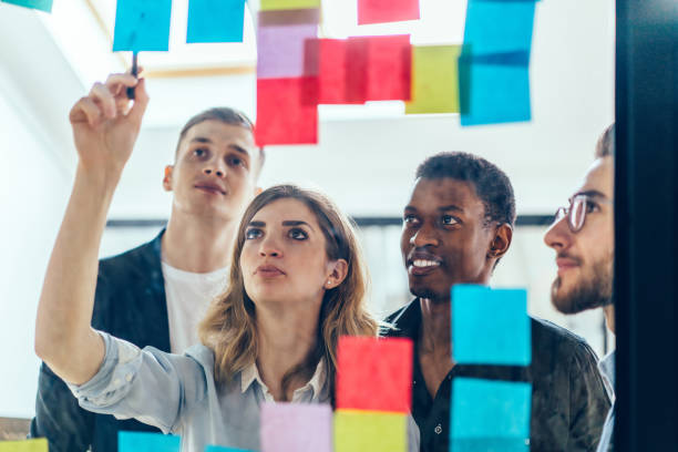 istock Multicultural group of male and female designers collaborating on project using colorful stickers with ideas for productive work.Positive colleagues reading notes written on papers glued on glass wall 1167050267