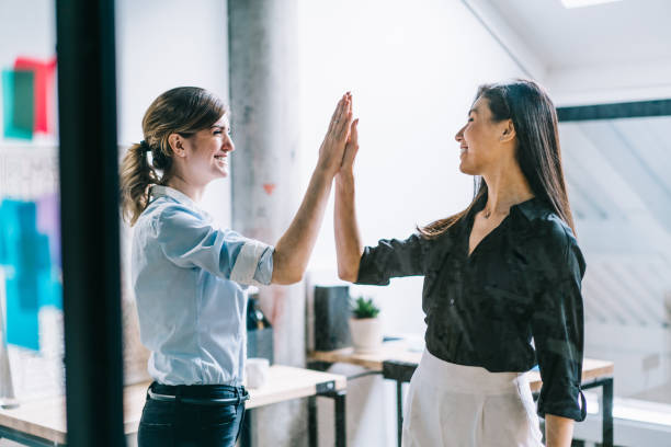 istock Two professional positive colleagues celebrating success of teamwork on common task standing behind glass wall in modern office.Female designers giving five each other after productive great job 1167050401