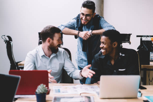 istock Positive male colleagues having fun during teamwork on design project sitting at table with laptops in modern office.Cheerful friends laughing during break working together in finance company 1167050415