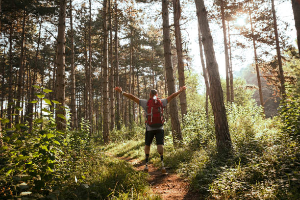 istock Hiker with artificial limbs and hiking poles against sun with raised arms 1167053304