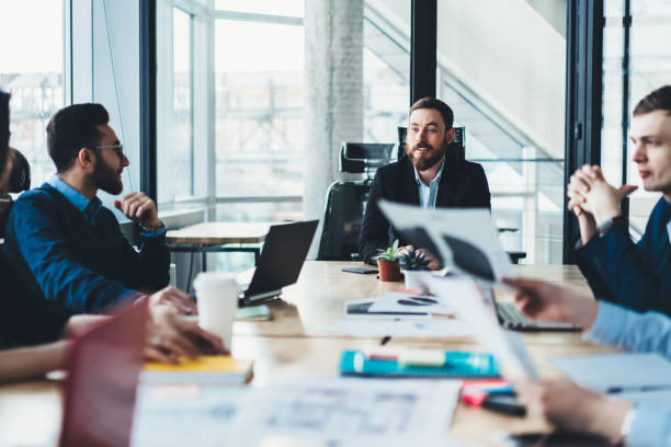istock Male proud ceo talking with experienced employees and discussing ideas for successful project sitting at meeting table in modern office.Executive manager teamworking with creative young people 1167058070