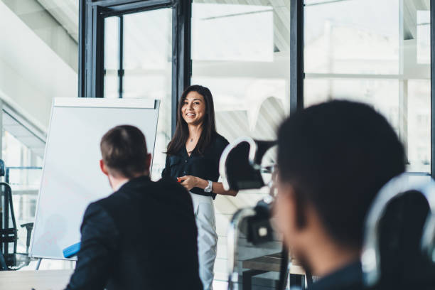 istock Positive successful female trader talking about financial reports during briefing in office.Cheerful young woman coach conducting business workshop for young entrepreneurs standing near flip chart 1167058087