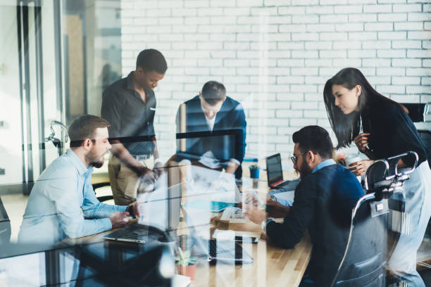 istock Diverse young people in formal wear communicating with each other and discussing creative ideas for developing design project sitting at meeting table behind glass wall in stylish office interior 1167058118