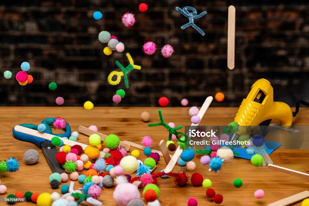 Crafting And Scrapbooking Supplies Falling To A Wooden Table Work Surface  In A Rainfall Of Colorwith Pompoms Sticks Pipecleaners And Yarn In A  Rainbow Of Colors All Together With Several Crafting Tools