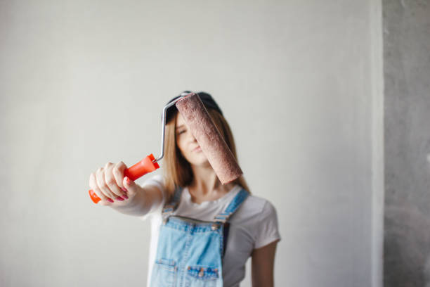 istock Selective focus at painting roller in young Caucasian woman hand in front of a reparing new wall in a room. 1167060708