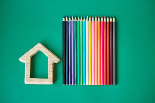 Wooden house figurine and several colored pencils isolate on green background, concept back to school, selective focus