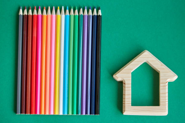 istock Wooden house figurine and several colored pencils isolate on green background, concept back to school, selective focus 1167070138