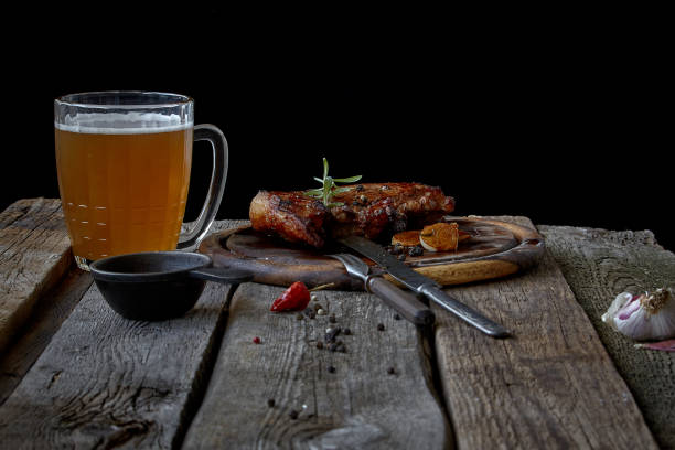 Still life with a big fried steak, a glass of beer, mustard and cutlery on an old wooden tabletop, the concept of Beer Fest and St. Patrick's Day Still life with big fried steak, a glass of beer, mustard and cutlery on an old wooden tabletop, the concept of Beer Fest and St. Patrick's Day steak-and-ale stock pictures, royalty-free photos & images