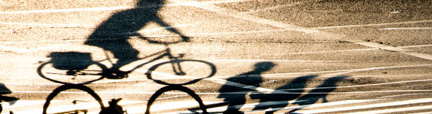 verschwommene schattensilhouette einer person, die mit dem fahrrad fährt, und fußgängern, die die straße mit straßenmarkierungen überqueren - rules of the road stock-fotos und bilder