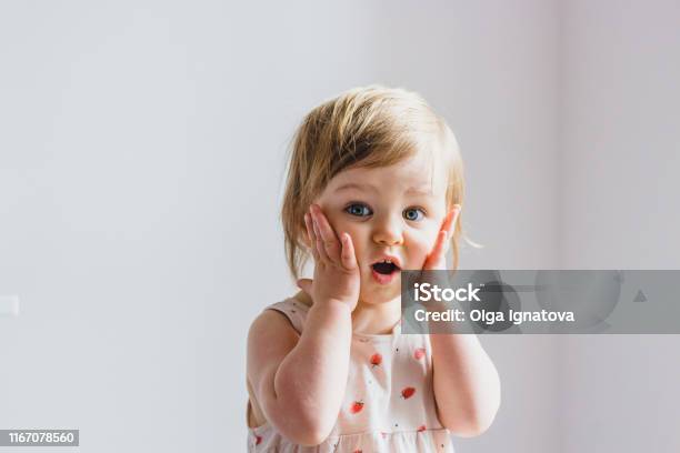 Surprised Shocked Child Toddler Girl With Hands On Her Cheeks Isolated On Light Background Stock Photo - Download Image Now