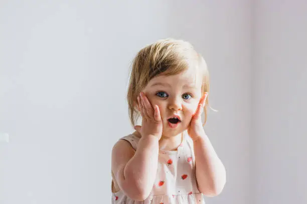 Photo of Surprised shocked child toddler girl with hands on her cheeks isolated on light background