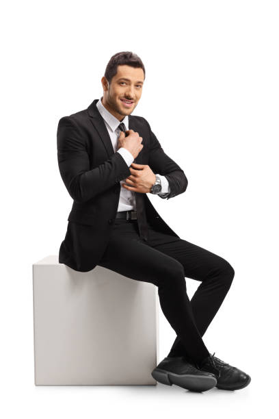 istock Young man in a suit sitting and fixing his tie 1167079975