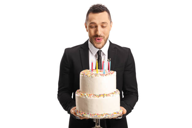 バースデーケーキを持ち、ろうそくを吹くスーツを着た若者 - cake birthday candle blowing ストックフォトと画像