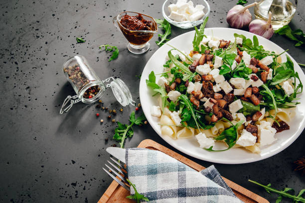 side view of a plate with food. a dish of pasta, rucola and spices, next to the ingredients of food, garlic, tomatoes on a stone, dark countertop. - asia cooked food gourmet imagens e fotografias de stock