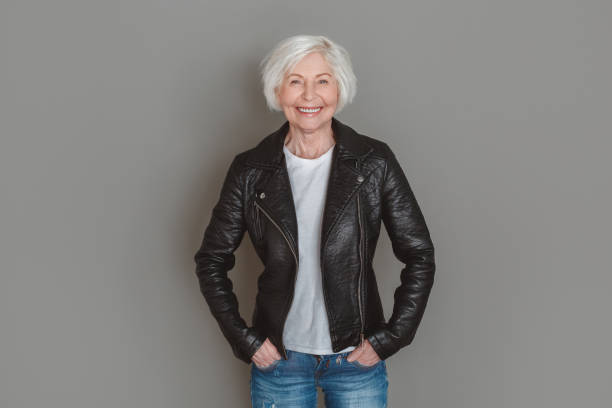 istock Senior woman in leather jacket studio isolated on grey wall hands in pockets happy 1167097242