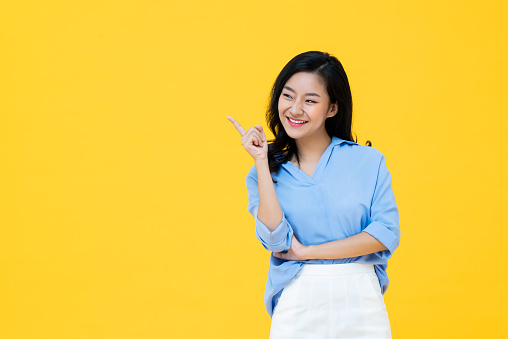 Attractive Asian woman confirming with her finger pointing isolated on yellow studio background with copy space