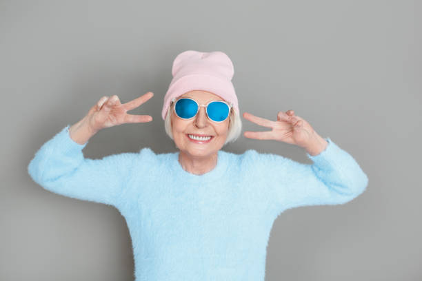 Senior woman in sweater and hat studio isolated on grey wall cool