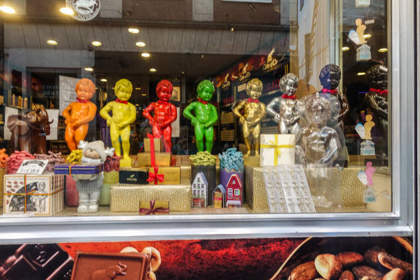 Brussels, Belgium - June 22, 2019: Large chocolate Manneken Pis statues in different colors posing on top of collection of chocolat gifts in window of confectionery store.