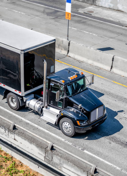 istock Black big rig day cab semi truck transporting black semi trailer driving on the interstate highway 1167100020