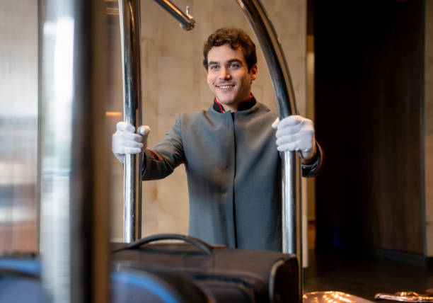 Young bellboy at a hotel moving luggage cart to a guest room very cheerfully Young bellboy at a hotel moving luggage cart to a guest room very cheerfully and smiling concierge photos stock pictures, royalty-free photos & images