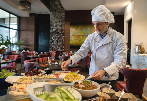 Handsome male chef checking the salad bar at a luxury hotel - Hotel occupation concepts