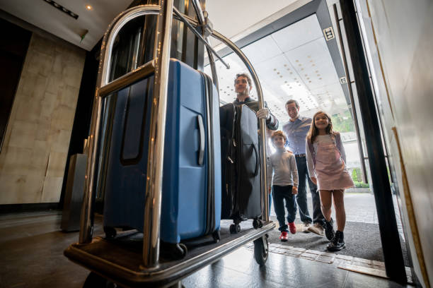 przyjazny bellhop pchający wózek z bagażem rodzinnym gościa na wózku gotowym do zameldowania w hotelu - hotel zdjęcia i obrazy z banku zdjęć