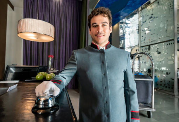 Handsome concierge ringing the bell on hotel counter while smiling at camera Handsome concierge ringing the bell on hotel counter while smiling at camera very happy hotel occupation concierge bell service stock pictures, royalty-free photos & images