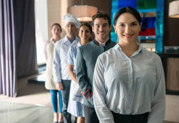 Female hotel manager and her team standing behind her all smiling at camera Female hotel manager and her team standing behind her all smiling at camera very happy bellhop photos stock pictures, royalty-free photos & images